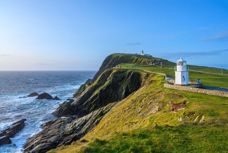 A white lighthouse on a cliff with rocks and sea below