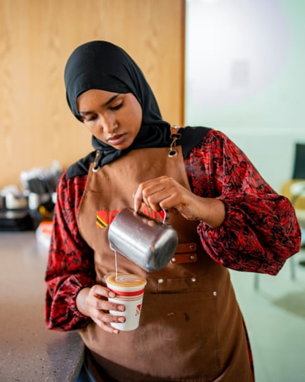 A young somali woman pouring milk into a takeout coffee cup