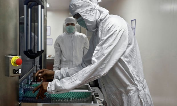An employee in PPE removes vials of AstraZeneca vaccine from a visual inspection machine inside a lab at Serum Institute of India.
