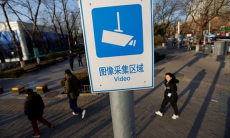 People walk past a video surveillance sign in Beijing