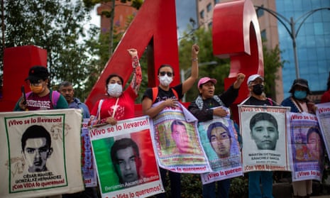 A group of people standing in a plaza hold signs bearing images of the students who were abducted in 2014.