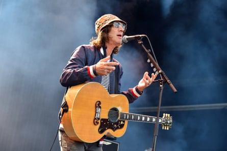 A man with a bucket hat and a guitar singing into a microphone