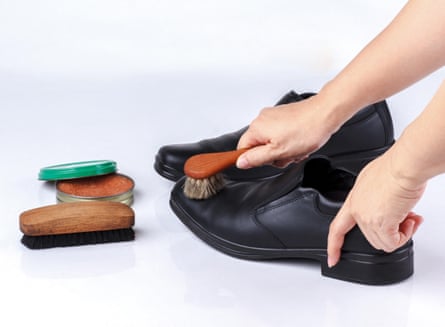 woman’s hand polishing black leather shoes with shoe brush on white background