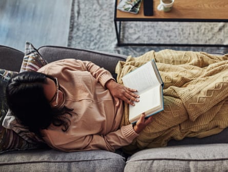 High angle shot of a young woman reading a book on the sofa at home