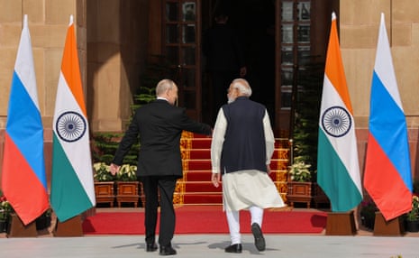 Vladimir Putin (L) and Narendra Modi (R) converse and walk toward a red-carpeted staircase that has an Indian flag and a Russian flag on either side of it.
