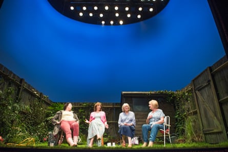Four women sitting in garden chairs in a row in a garden setting on stage.