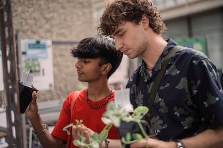 Two young men hold small pots of plants.