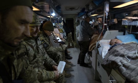 Wounded soldiers are evacuated on a specially adapted bus: some sit on a bench, still wearing helmets and fatigues, while others are lying on beds under blankets and attached to drips and medical equipment