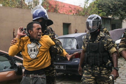 Man is held by security forces wearing protective gear and helmets.