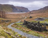 A view of an abandoned slate quarry amid a rugged landscape in Snowdonia (Eryri national park), with a lake in the background.
