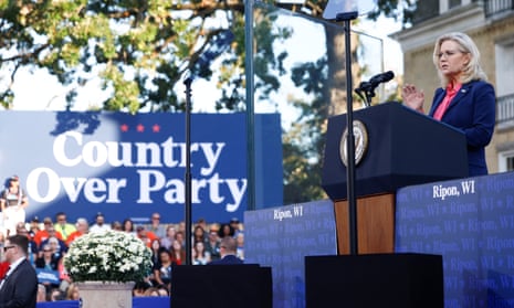 woman wearing blue suit and pink shirt stands behind podium as crowd looks at her