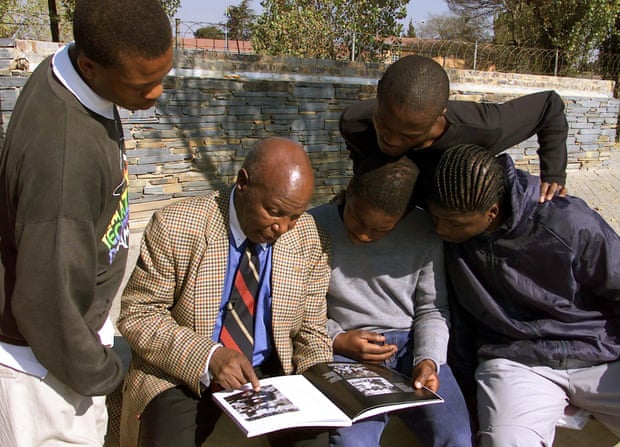 Teenagers look on in 2001 as veteran photojournalist Alf Khumalo, who died in 2012, shows them photographs of a burning building near their Soweto school during the uprising.