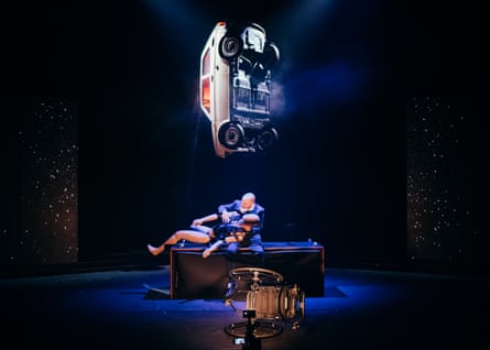Mark on stage, cradling a crash dummy, his wheelchair flipped, a car dangling above him