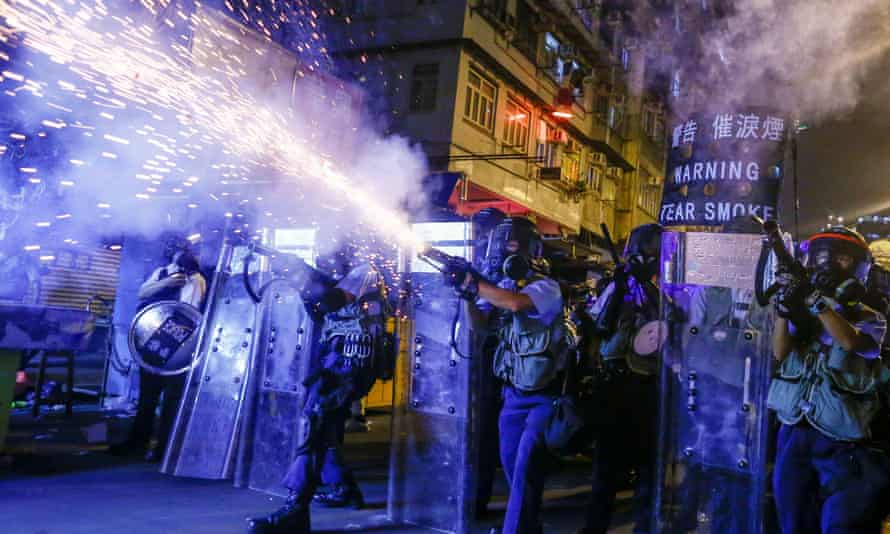 Nighttime picture of group of police in riot gear and shields, firing a device emitting a shower of sparks