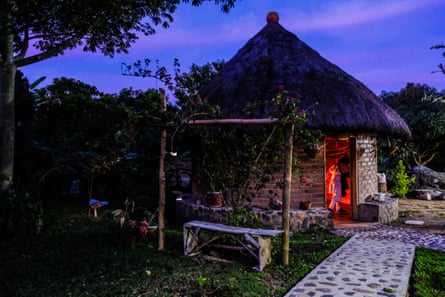 A round brick hut with a thatched roof sits in a landscaped garden