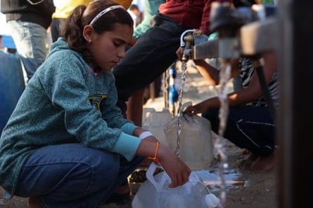 A girl holds a container as water pours into it from a tap