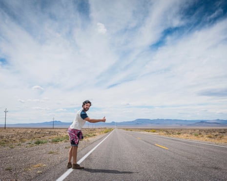 Man hitchhiking on a remote road, beneath a cloudy sky