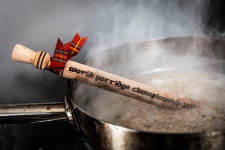 A wooden spurtle sitting in a pot of simmering oats.