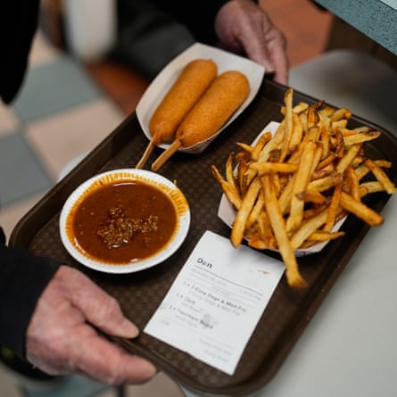 A customer with a tray of breaded hotdogs on sticks, fries and chili