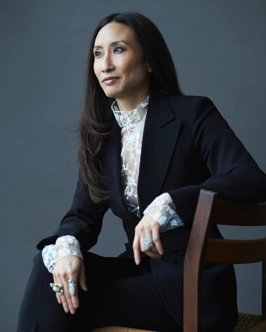 Elizabeth von der Goltz sitting sideways on a wooden chair in a smart blue fitted suit, white lacy blouse, and large rings