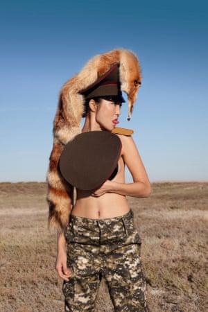 Bare-chested model partially clad in a uniform inspired by the Khazak Republican Guard, an epaulet affixed to her exposed shoulder. She seems to peer directly at the face of the skinned fox hanging downward from her hat