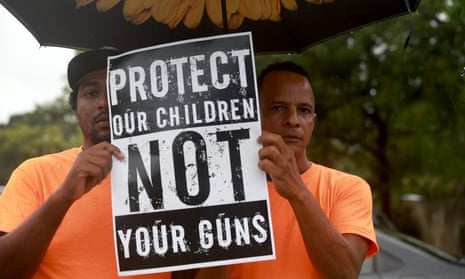 Two men wearing orange shirts stand under an umbrella holding a sign that says 'Protect our children, not your guns'.
