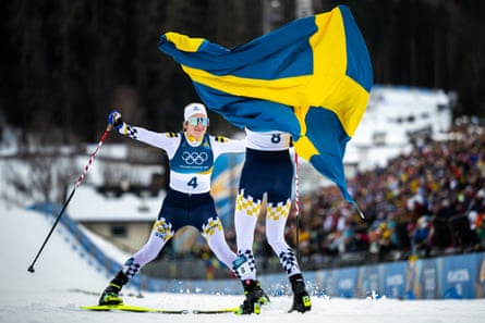 Ebba Andersson slides towards Frida Karlsson, who is draped in a Sweden flag.