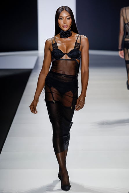 Naomi Campbell walks on the catwalk wearing a black bra and pants half-covered by a sheer dress