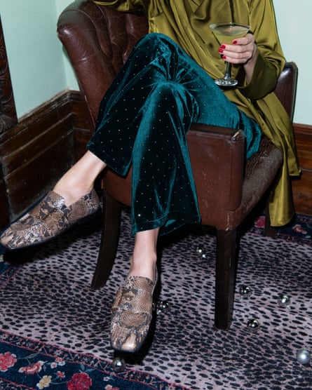 model sits with legs crossed over the arm of a leather armchair