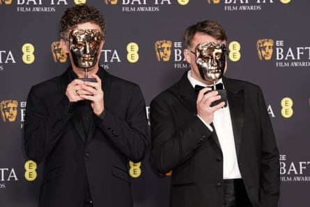 The two film-makers holding the Bafta award masks over their faces