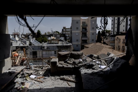 An apartment destroyed by an Iranian missile strike: it is framed by walls in black shadow with sofas, furnishings and rubble open to the clear sky behind.