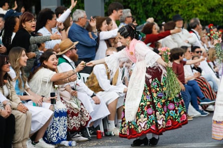 A woman in traditional folk costume hands a spectator a flower