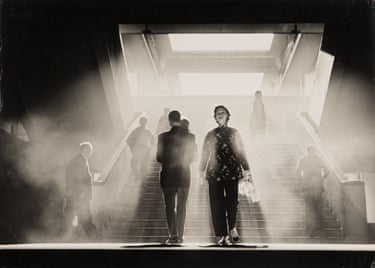 Silhouetted figures ascend a smoky, light-streaked staircase towards a bright doorway in Hong Kong