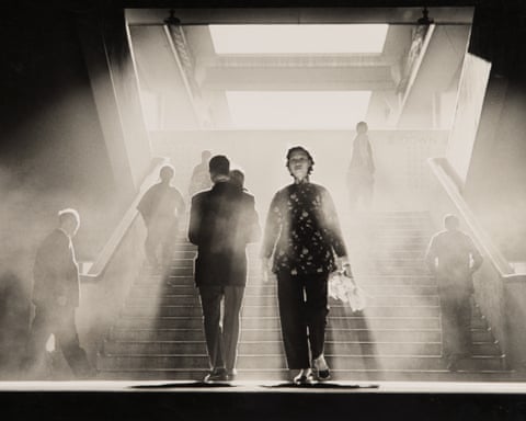 Silhouetted figures walk down a hazy, sunlit staircase through thick fog or smoke
