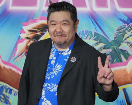 Eric Bauza, in a black blazer over a floral shirt, gives a peace sign at a premiere.