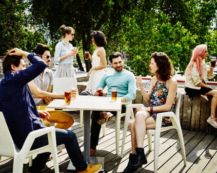 Friends talking and sharing drinks at party on rooftop deck on sunny afternoon