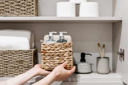 Woman putting a wicker box with cosmetics products into a bathroom closet