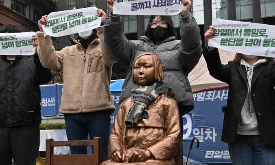 South Korean protesters hold up banners beside a statue of a teenage girl symbolizing 'comfort women' near the Japanese embassy in Seoul in March 2021