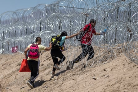 Migrants walk through razor wire surrounding a makeshift migrant camp after crossing the border from Mexico