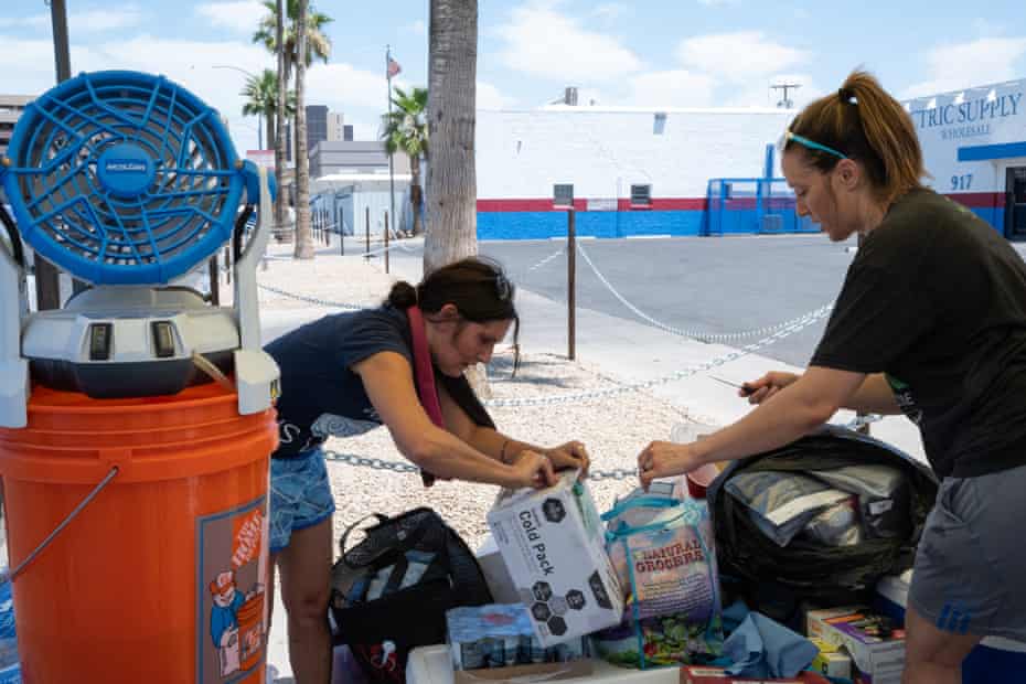Stacey Champion, left, and Nicole Rodriguez pass out water and cooling towels to unsheltered neighbors staying in The Zone, an encampment where conservative estimates say 900 people stay, during an excessive heat warning where the temperature reached 114°F on June 11, 2022 in Phoenix, Ariz. Champion organizes people to take action and contact elected officials and utility companies to advocate for people struggling to stay safe and cool during extreme heat.