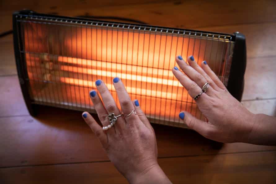 Caitlin Cassidy warms her hands by an electric radiant bar heater in her home