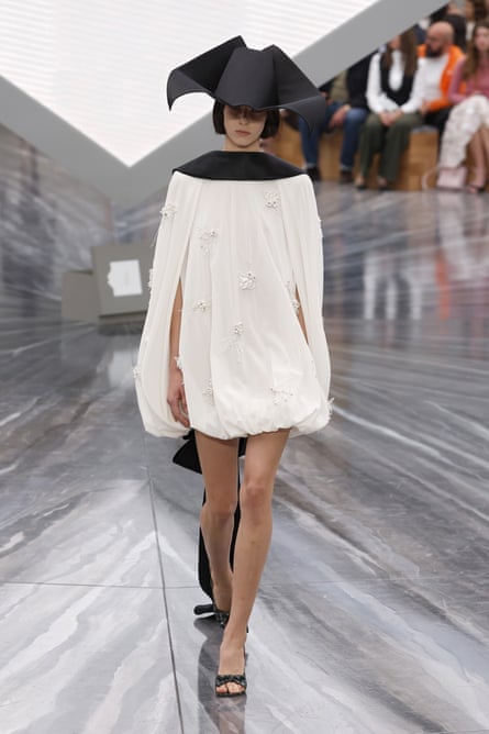 A model in a pointy black hat and short cream puffball dress
