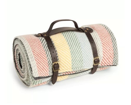 A rolled and strapped wool picnic rug. The rug is chevron striped in a pastel red green and yellow.