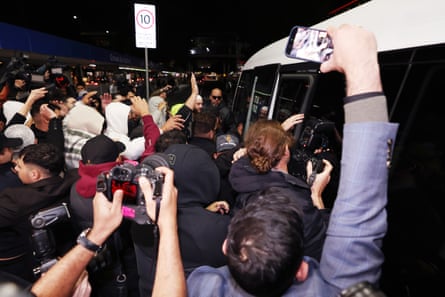 A group of supporters gather around a bus carrying the returnees away from Melbourne airport.