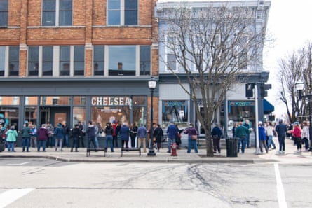 Street view showing two lines of people standing on a pavement with shopfronts behind them.