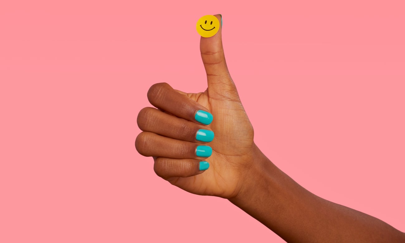 Thumbs-up hand with turquoise-painted nails and smiley sticker on thumb, against pink background