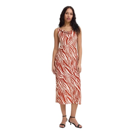 A model wears a cowl neck midi dress. The tiger stripe pattern is brick and cream patterned. The model has hair past their shoulders and wears small strappy black heels.