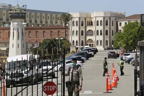 An officer closes the main gate at San Quentin state prison. The prison building in the background includes a guar's watch tower.