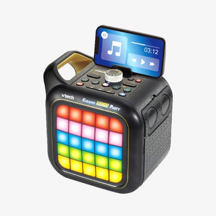 A VTech karaoke speaker with colourful lit grid buttons holds a smartphone showing a music player