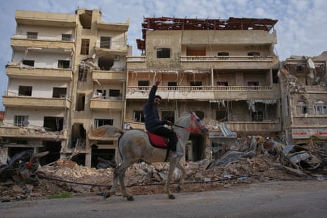 A man rides a horse past the site of buildings destroyed in an airstrike.